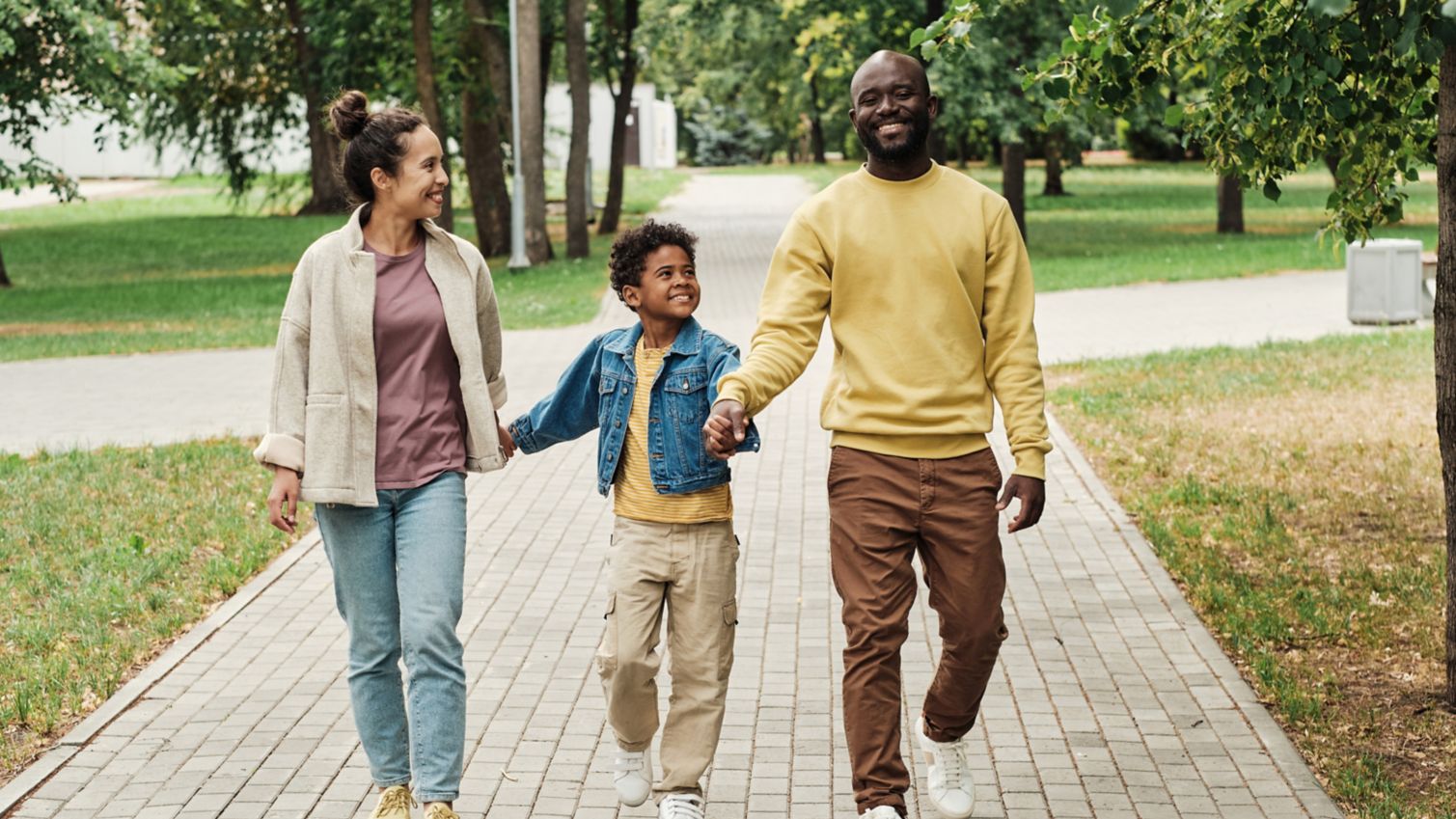 A family of 3 holds hands while they walk outside